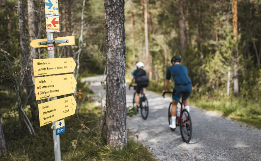 Radfahrer auf Waldweg neben Wegweiser im Wald