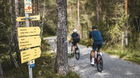 Werde zum GravelKING in Gravel.Tirol © Andreas Vigl Radfahrer auf Waldweg neben Wegweiser im Wald