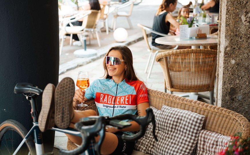 Woman in cycling gear relaxing with a drink at a café next to her bicycle