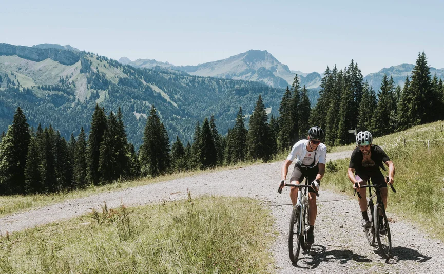 Zwei Radfahrer fahren auf einem Schotterweg in den Bergen bei Sonnenschein.