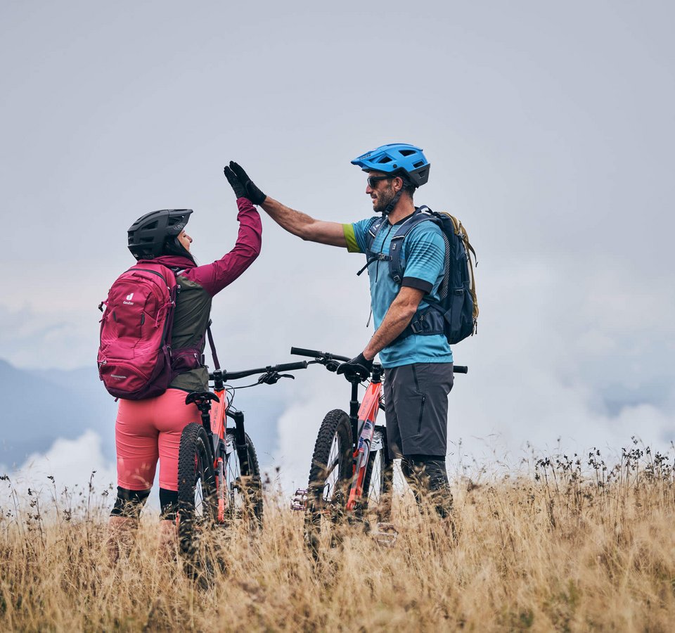 Zwei Mountainbiker geben sich auf einer Wiese einen High Five