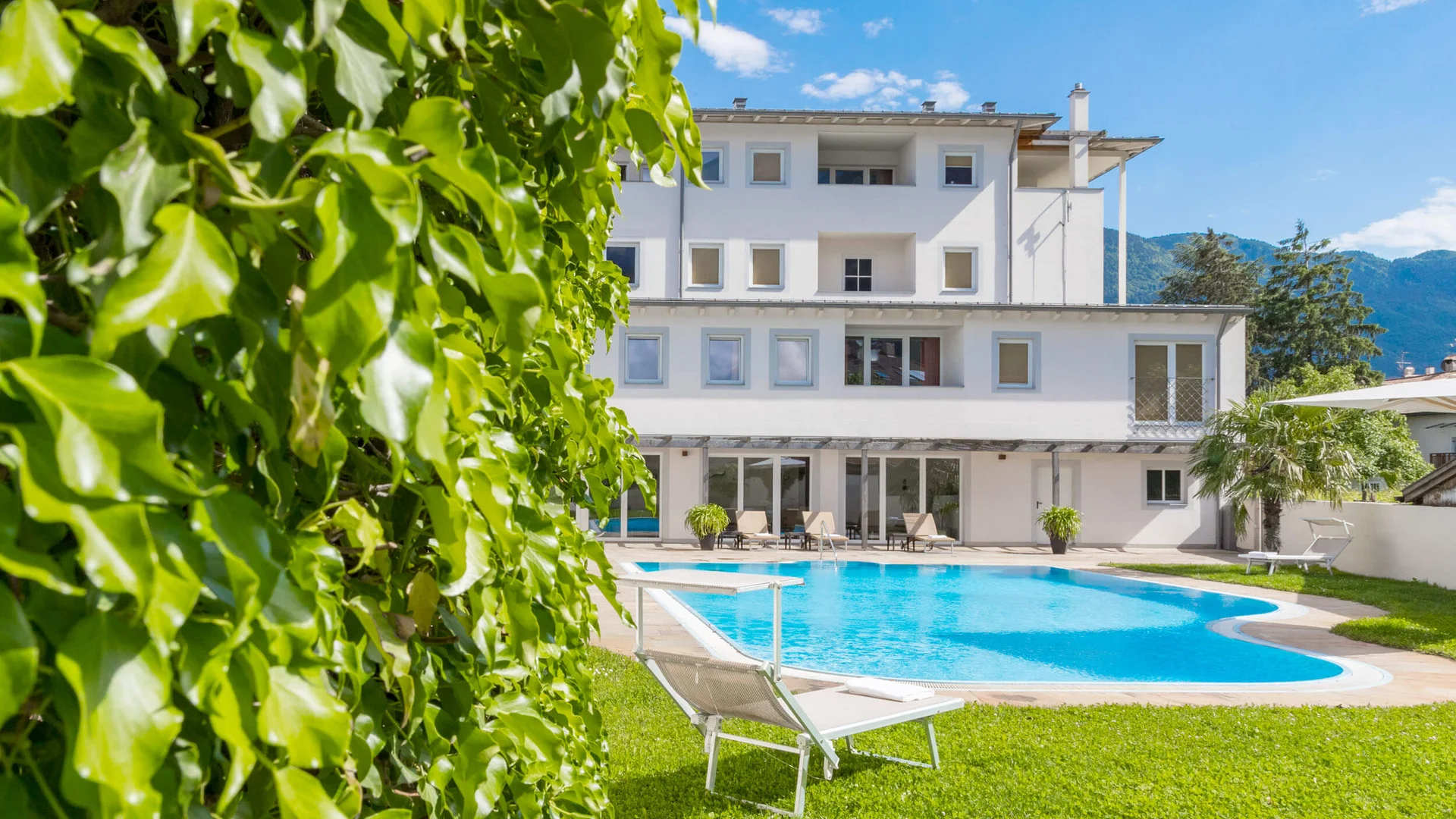 Weißes Gebäude mit Pool, Liegestuhl und grünem Rasen unter blauem Himmel