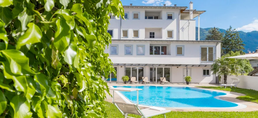 Weißes Gebäude mit Pool, Liegestuhl und grünem Rasen unter blauem Himmel