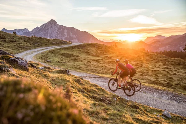 Destinations © Salzburger Land Tourismus Two cyclists riding on a winding mountain trail at sunset