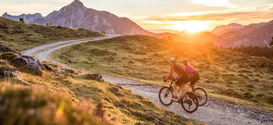 Gravelbike Urlaub im SalzburgerLand © Salzburger Land Tourismus Zwei Radfahrer fahren auf einem kurvigen Bergpfad bei Sonnenuntergang