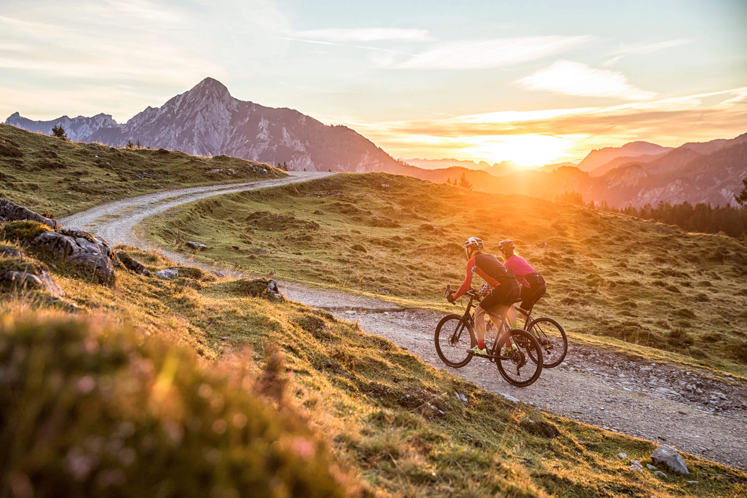 Destinationen © Salzburger Land Tourismus Zwei Radfahrer fahren auf einem kurvigen Bergpfad bei Sonnenuntergang