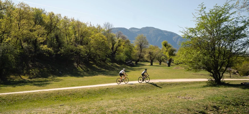 Auf Schotterkurs im Hotel Teutschhaus © Cinemepic / Teutschhaus Zwei Radfahrer auf einem Weg durch grüne Landschaft mit Bergen im Hintergrund