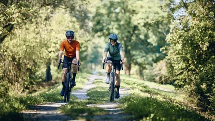 Zwei Radfahrer fahren auf einem grasbewachsenen Waldweg