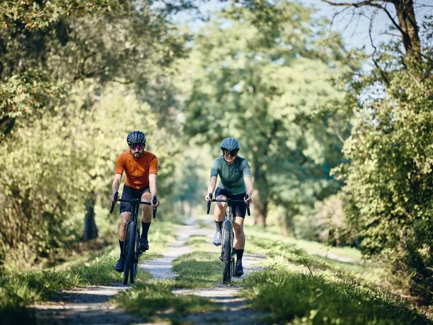 Zwei Radfahrer fahren auf einem grasbewachsenen Waldweg