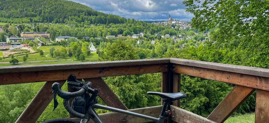 Fahrrad auf Holzplattform mit Blick auf grünen Hügel und bewölkten Himmel