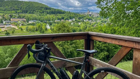Fahrrad auf Holzplattform mit Blick auf grünen Hügel und bewölkten Himmel