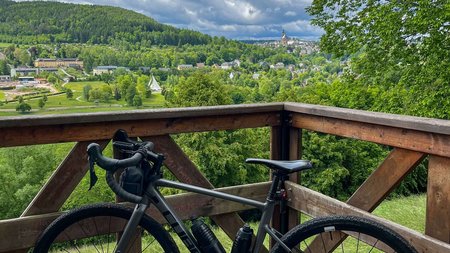 Fahrrad auf Holzplattform mit Blick auf grünen Hügel und bewölkten Himmel
