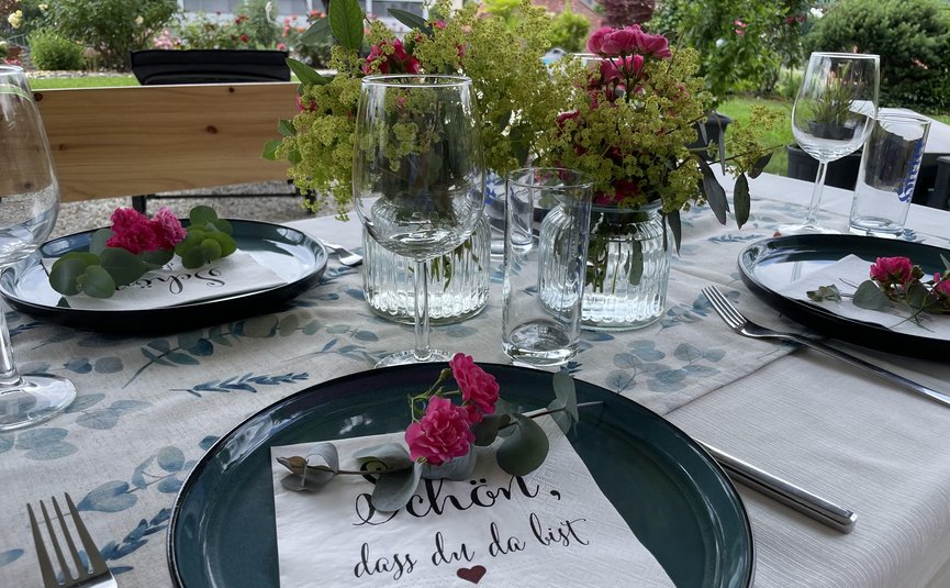 Gedeckter Tisch mit Blumen und Serviette mit Willkommensgruß im Garten