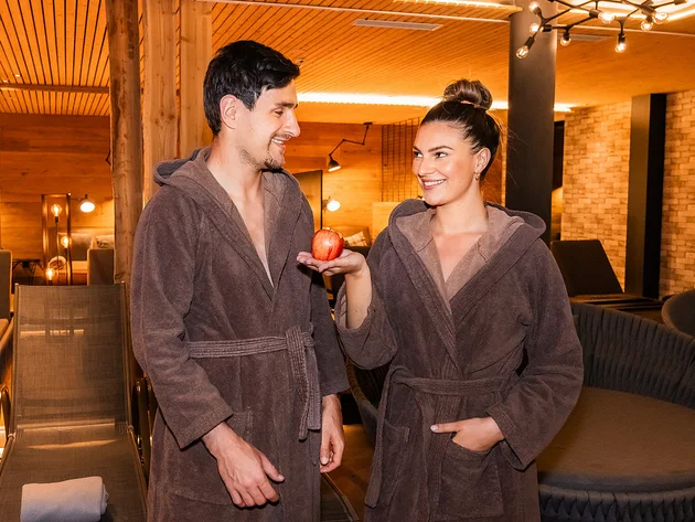 Paar in Bademänteln im Spa, Frau hält roten Apfel
