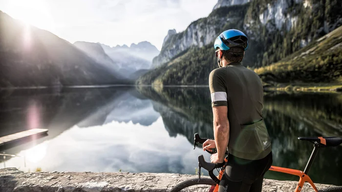 Cyclist looking at calm mountain lake at sunrise