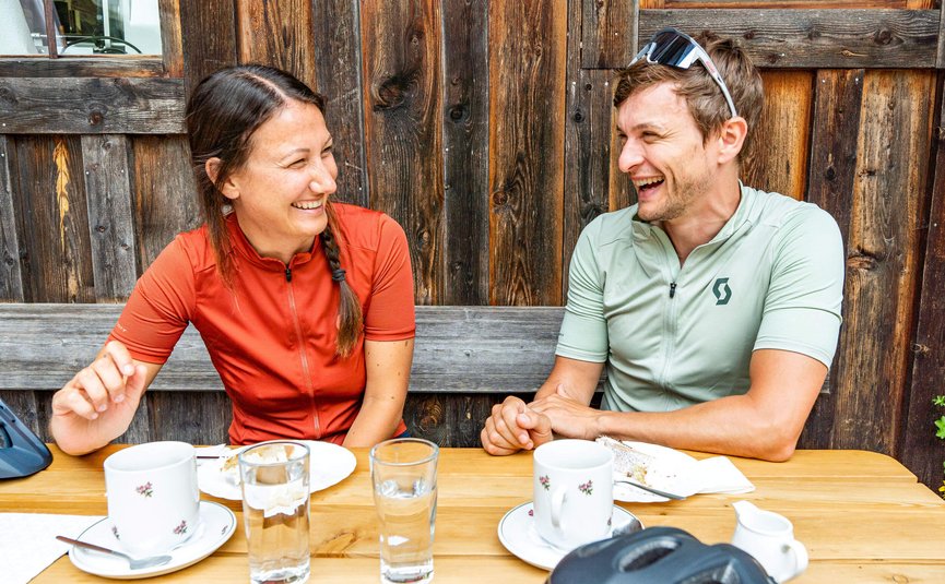 Biohotel Rupertus **** © Saalfelden Leogang Touristik - Yvonne Hörl Zwei lachende Radfahrer sitzen draußen am Holztisch mit Kaffeetassen