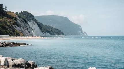 Küste mit Felsen, Strand und blauem Meer unter hellem Himmel