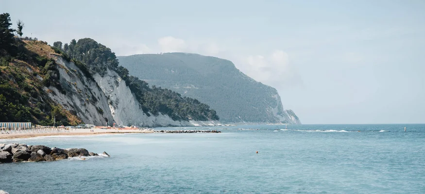Küste mit Felsen, Strand und blauem Meer unter hellem Himmel
