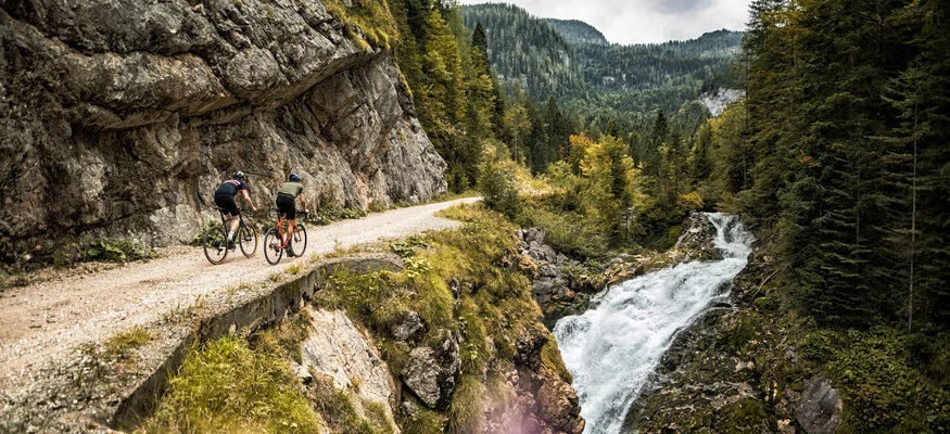 Fuschlseeregion © WOM Medien GMBH - Andreas Meyer Zwei Radfahrer auf einem Bergweg neben Wasserfall und Wald
