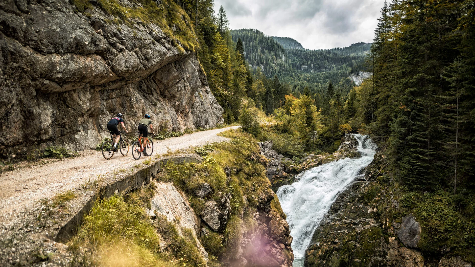 Qualitätsversprechen © WOM Medien GMBH - Andreas Meyer Zwei Radfahrer auf einem Bergweg neben Wasserfall und Wald