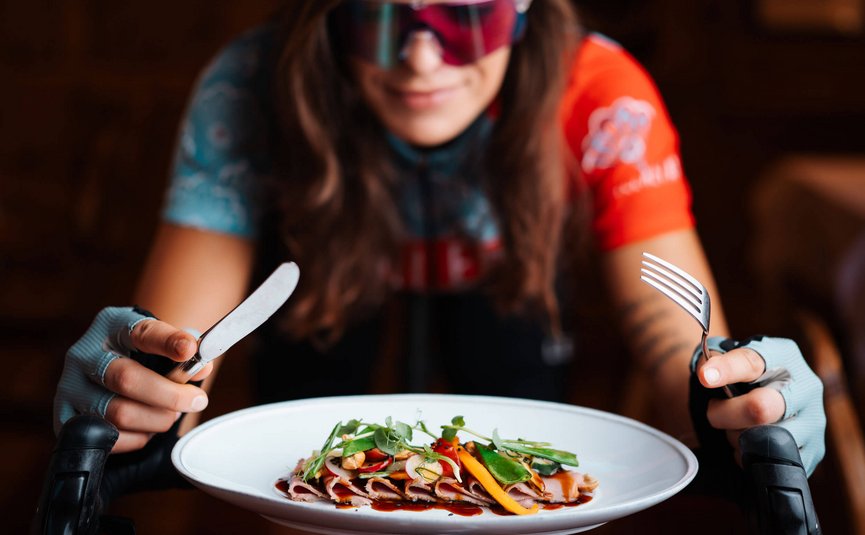 Woman on racing bike holding plate and cutlery, ready to eat