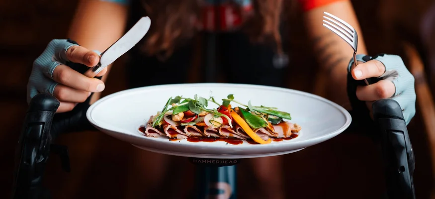 Woman on racing bike holding plate and cutlery, ready to eat