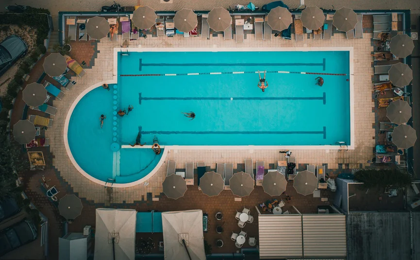 Vogelperspektive auf einen Schwimmbeckenbereich mit Sonnenschirmen und Menschen