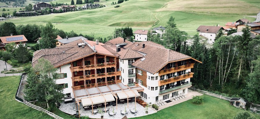 Blick auf ein Hotel im Bergtal mit grünen Wiesen und Bergen im Hintergrund