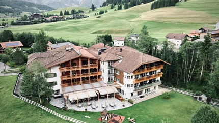 Blick auf ein Hotel im Bergtal mit grünen Wiesen und Bergen im Hintergrund