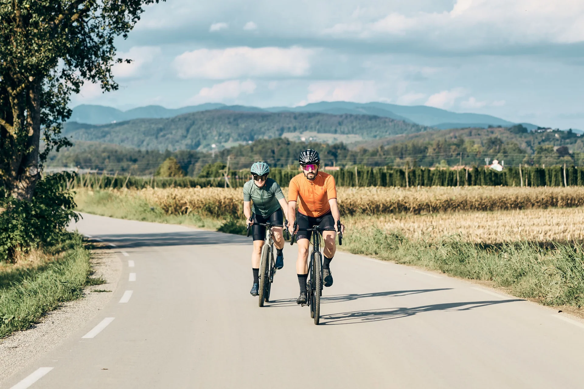 Gravelbike Holidays © Tobias Köhler Zwei Radfahrer fahren auf einer Landstraße mit Berge und Felder im Hintergrund