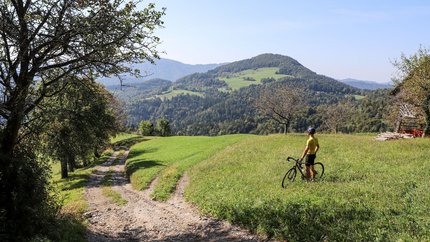 Špilk © Kaja Ribezl Radfahrer steht auf Wiese und blickt auf bergige Landschaft