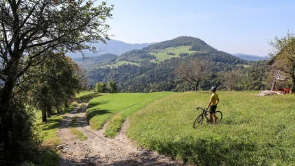 Radfahrer steht auf Wiese und blickt auf bergige Landschaft