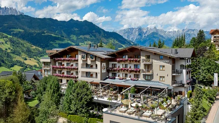 Hotel Alpendorf mit Terrasse in bergiger Landschaft bei Sonnenschein