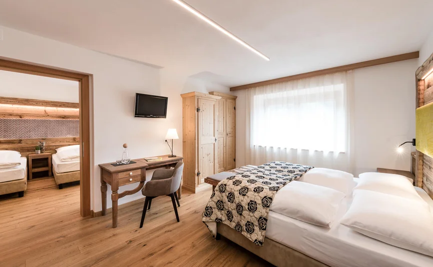 Helle Hotelzimmer mit Doppelbett und angrenzendem Zimmer mit zwei Einzelbetten