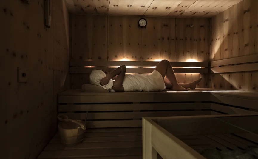 Person relaxing in sauna wrapped in towel with covered head lying down