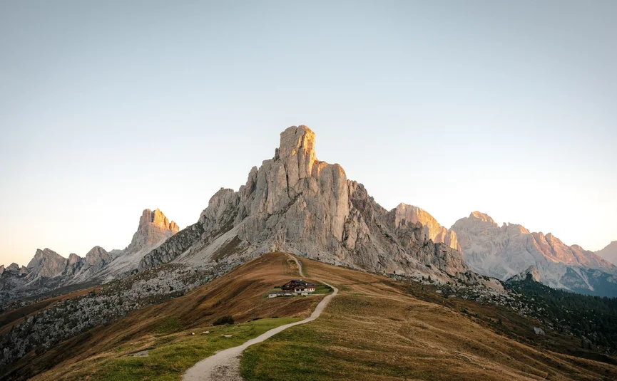 Trail leading to mountain hut below rocky peak at sunset