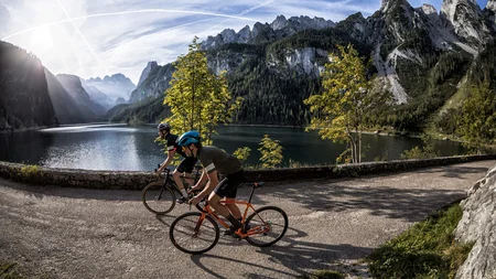 Zwei Radfahrer fahren an einem Bergsee mit Bergen im Hintergrund