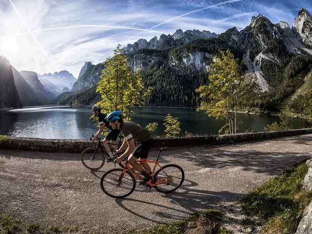 Zwei Radfahrer fahren an einem Bergsee mit Bergen im Hintergrund