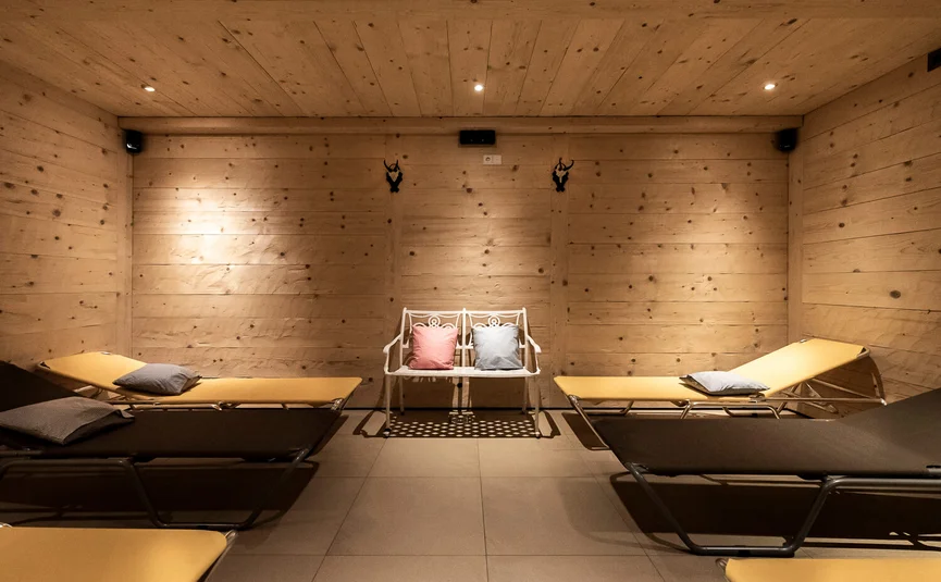 Relaxation room with wooden walls, loungers and white bench with colorful pillows