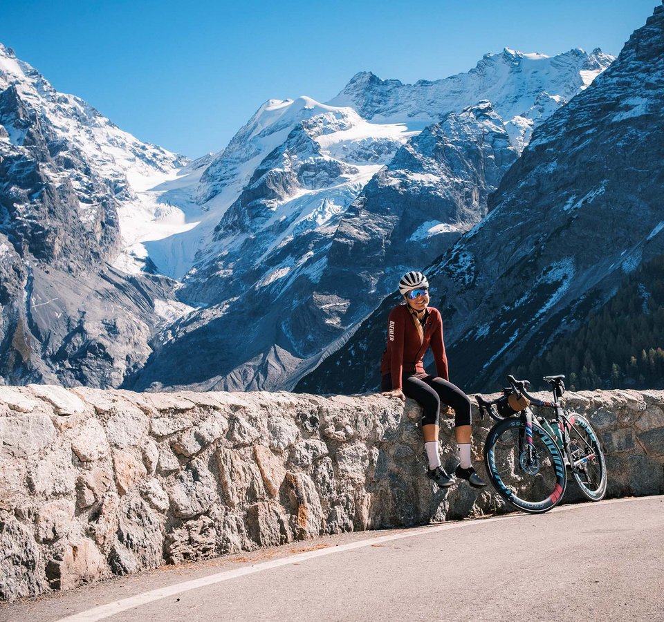 Checklist für das Bikepacking-Abenteuer © Maria Wilke Frau mit Fahrrad sitzt auf Steinmauer vor schneebedeckten Bergen