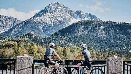 Zwei Radfahrer blickend auf schneebedeckten Berg und bewaldete Hügel