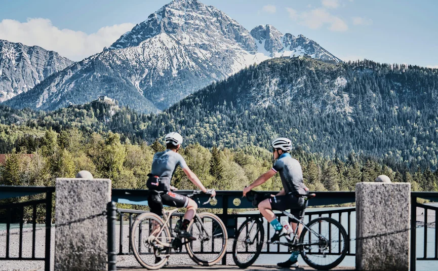 Zwei Radfahrer blickend auf schneebedeckten Berg und bewaldete Hügel