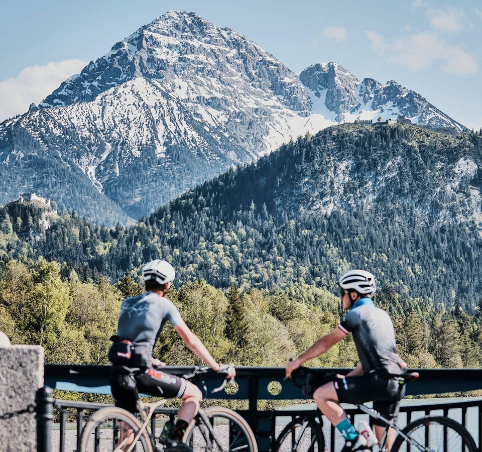 Zwei Radfahrer blickend auf schneebedeckten Berg und bewaldete Hügel
