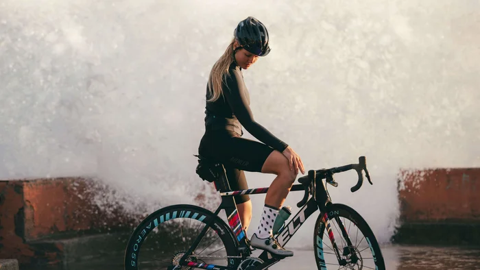 Checklist für das Bikepacking-Abenteuer © Maria Wilke Frau in Radbekleidung sitzt auf Rennrad vor Gischt am Meer