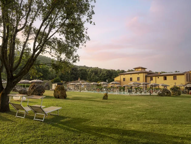 Gravelbiken in der Toskana © Hotel Casolare Le Terre Rosse Grüne Wiese mit Liegestühlen, Sonnenschirmen und gelbem Gebäude im Hintergrund