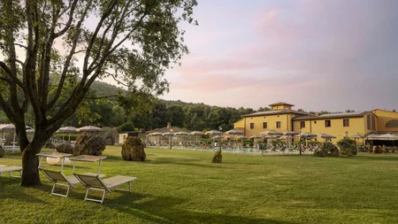 Gravelbiken in der Toskana © Hotel Casolare Le Terre Rosse Grüne Wiese mit Liegestühlen, Sonnenschirmen und gelbem Gebäude im Hintergrund