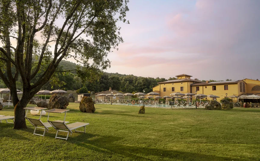 Green lawn with lounge chairs, umbrellas, and yellow building in the background