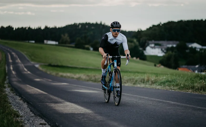 Radfahrer auf Landstraße mit grüner Wiese und Häusern im Hintergrund
