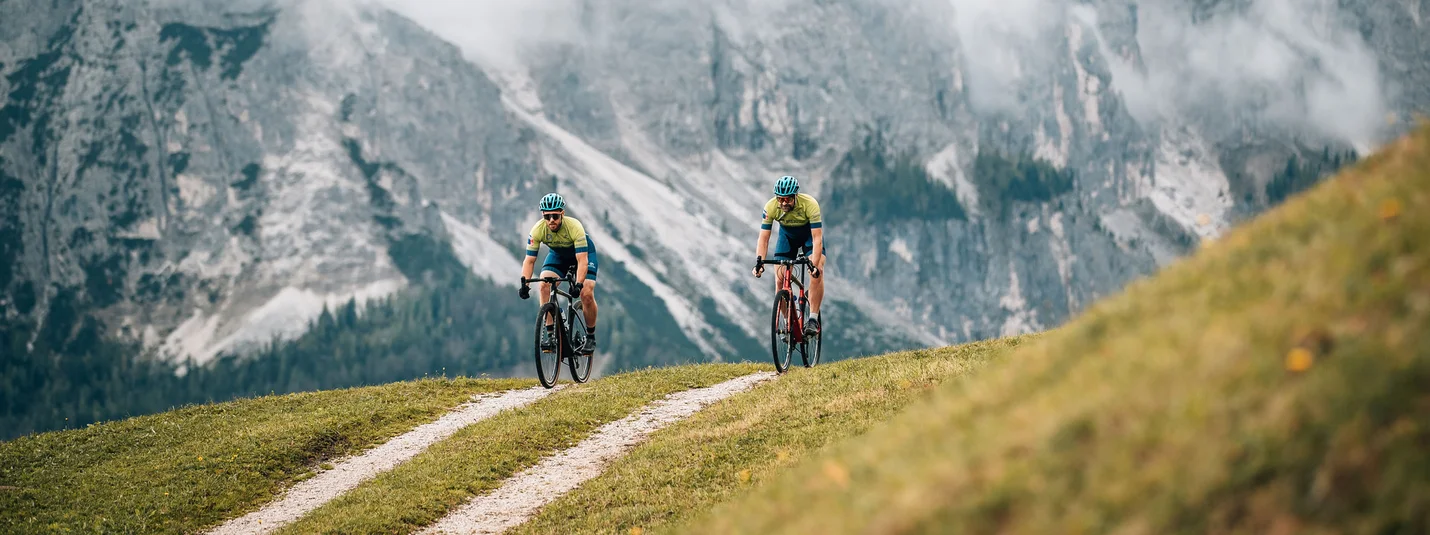Furkelpass round © Jens Scheibe Two cyclists riding on a mountain trail with misty alpine cliffs
