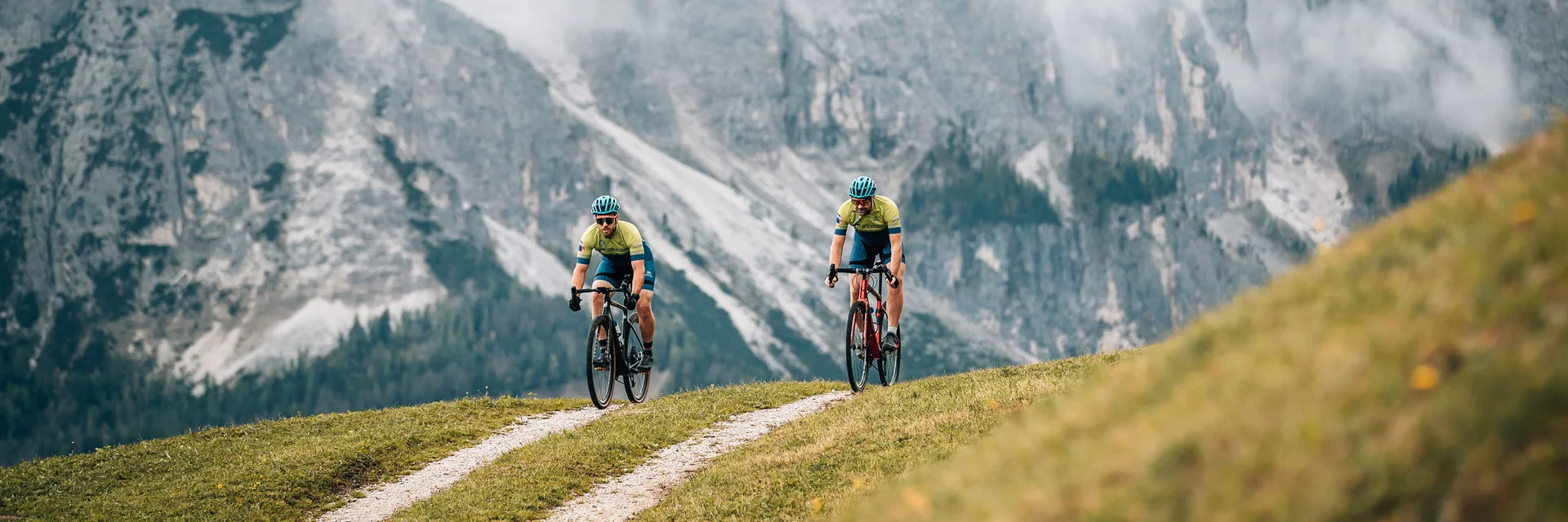 Zwei Radfahrer fahren auf einem Bergweg vor nebligen Alpenfelsen